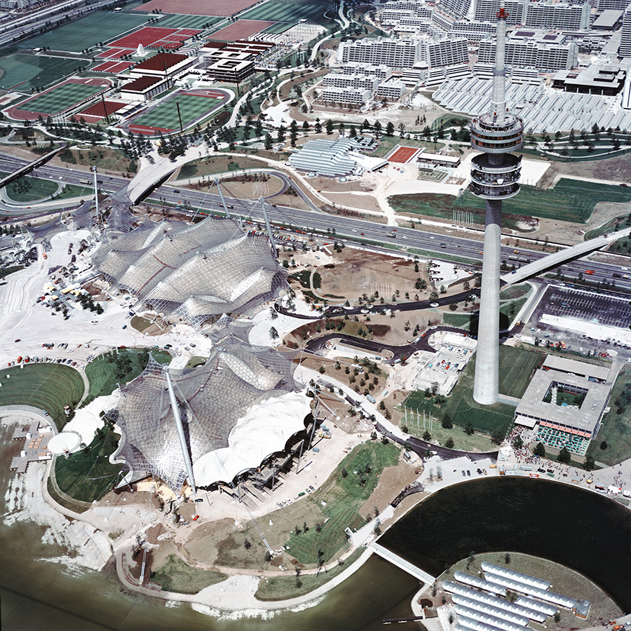 Das farbige Schrägluftbild zeigt das neu errichtete Olympiagelände mit Stadien, Turm, Sportplätzen und Olympischem Dorf.